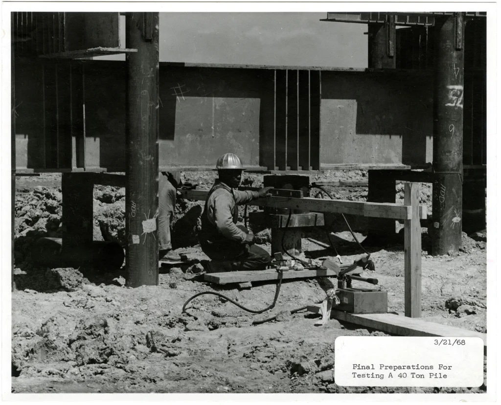 Hydraulic jack and dial gauges set up under a reaction frame for a pile load test
